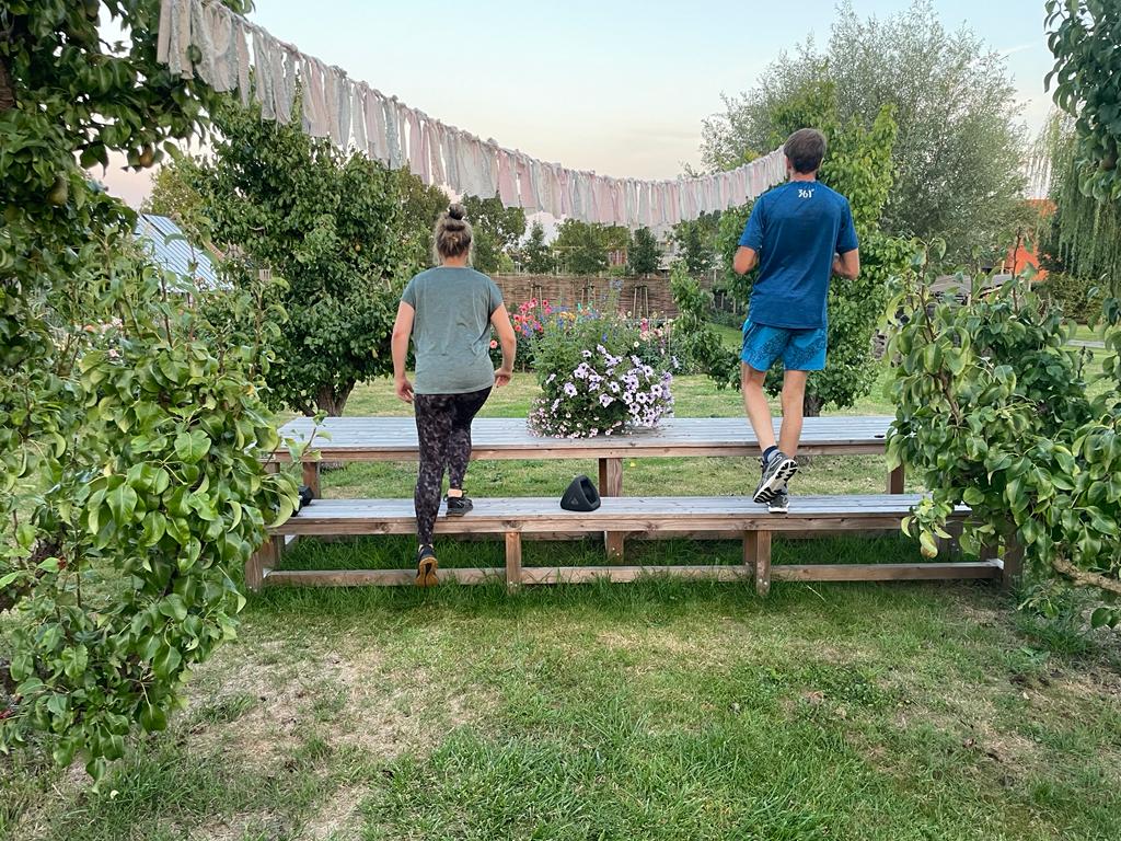 Man en vrouw trainen samen , in sportkleding, bij hun in de tuin. Stappen op een bankje voor het versterken van de beenspieren