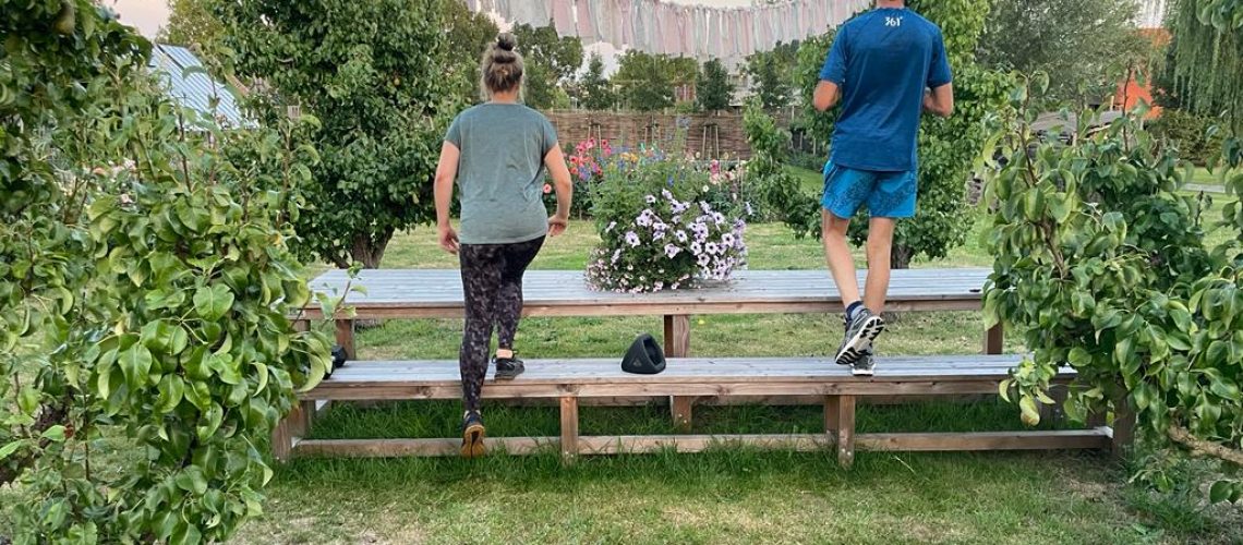 Man en vrouw trainen samen , in sportkleding, bij hun in de tuin. Stappen op een bankje voor het versterken van de beenspieren